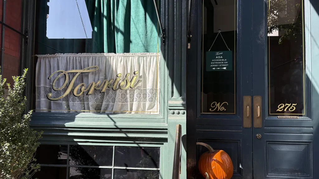 Entrance of Torrisi restaurant in NYC with green storefront, gold lettering, and ADA accessible sign.