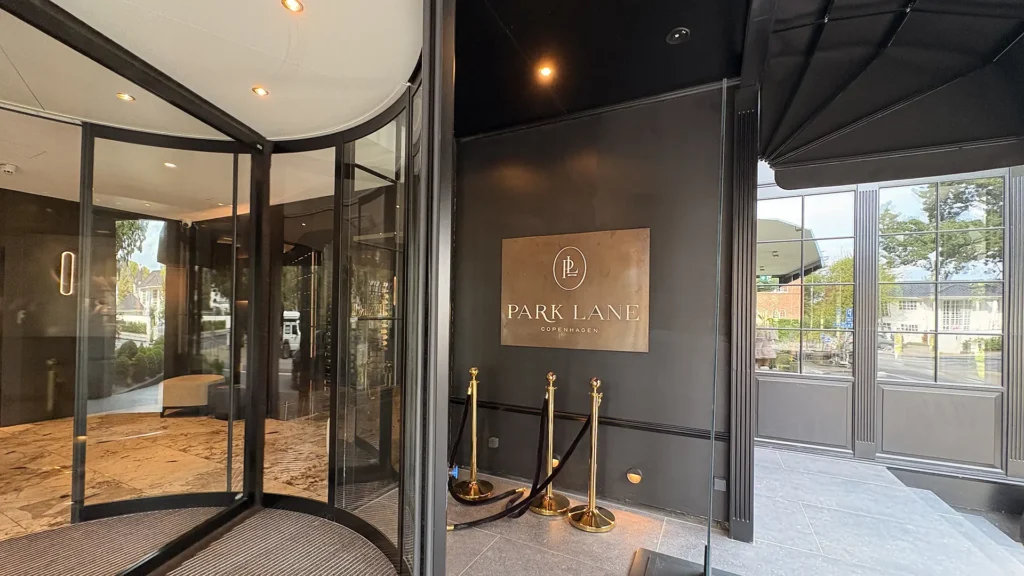 Entrance to Park Lane Copenhagen – the hotel’s modern glass entry with its logo displayed on a bronze plaque