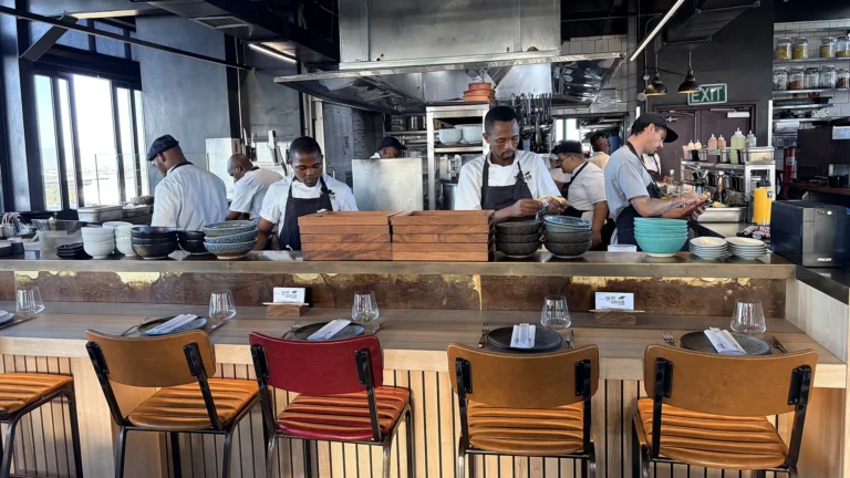 Open kitchen at The Pot Luck Club, Cape Town, with chefs preparing dishes behind the counter seating.